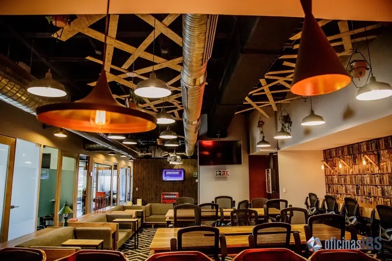 Área de coworking de IBS Santa Fe con mesas y lámparas colgantes
